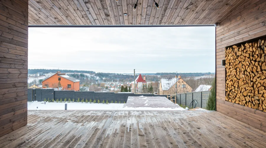 What Is Transparent Stain? - Cozy wooden deck with stacked firewood and scenic snowy village view in winter