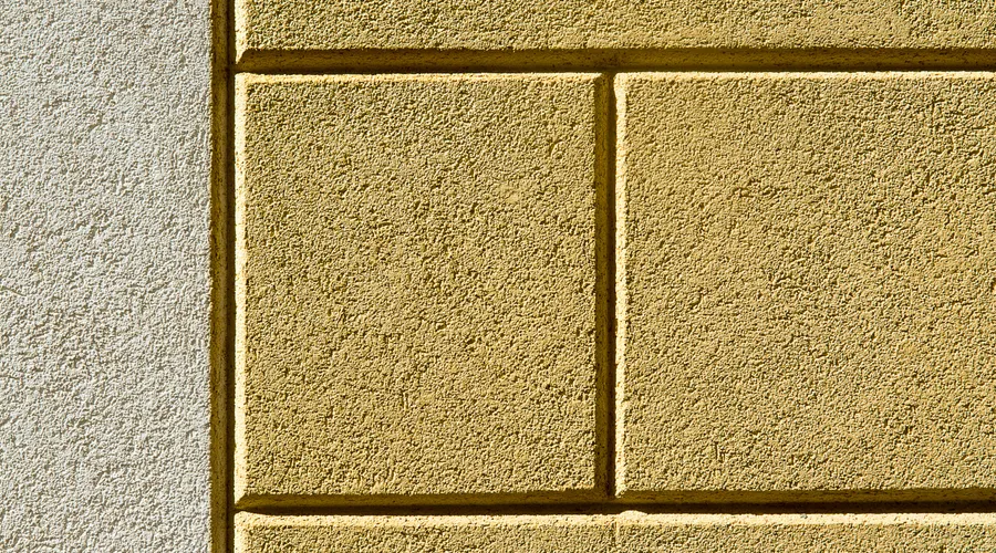 Elastomeric Coating - Detailed textured surface of a yellow painted cement wall with shadow effects