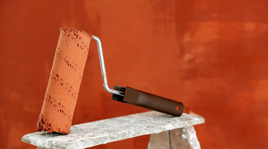 What Is a Drywall Sealer? - Detailed image of a paint roller resting on a ladder with a vibrant orange wall in the background