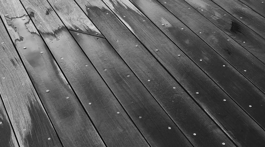 What Is Deck Sealer? - Close-up of a wet wooden floor with visible grain and screws in black and white